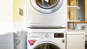 Una lavadora de carga frontal con un panel de control, un mueble pequeño debajo y un espejo encima.