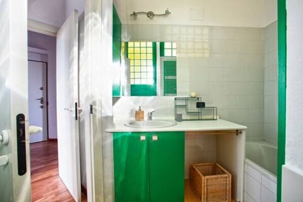 Een badkamer met een witte wastafel, een groen kastje en een raam met groene luiken.