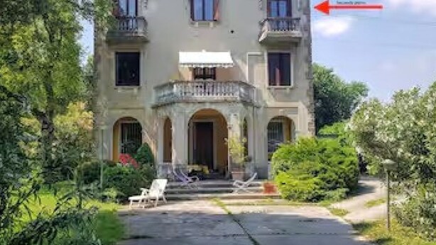Un edificio de dos plantas con un balcón, un acceso cubierto y un camino que lleva a la entrada.