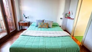Una cama con colcha verde, una mesita de noche con lámpara y una ventana con vistas.