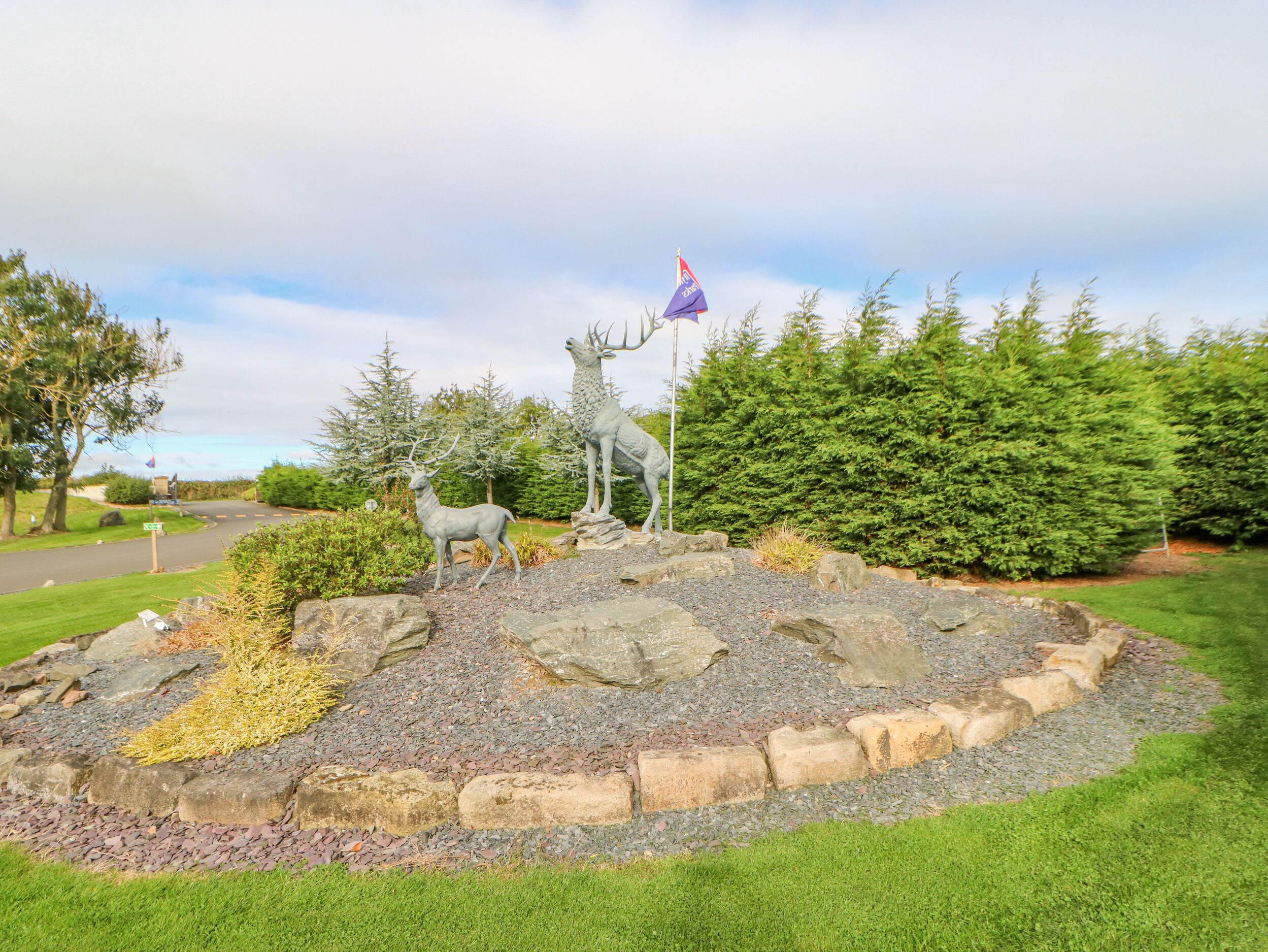 Un espace aménagé avec des statues de cerfs, un drapeau et une route en arrière-plan.