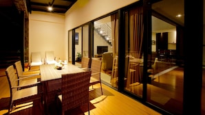 A dining area with wicker furniture, a table with a vase, and a view of a staircase leading to another room. - Kokol Haven Resort (Kota Kinabalu)