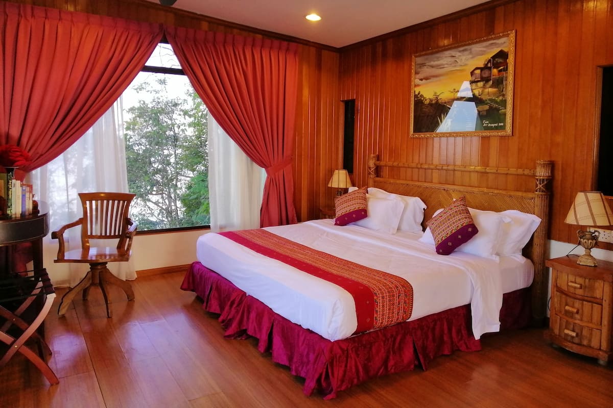 A hotel room with a large bed, wooden walls, a ceiling fan, and a window with red curtains.