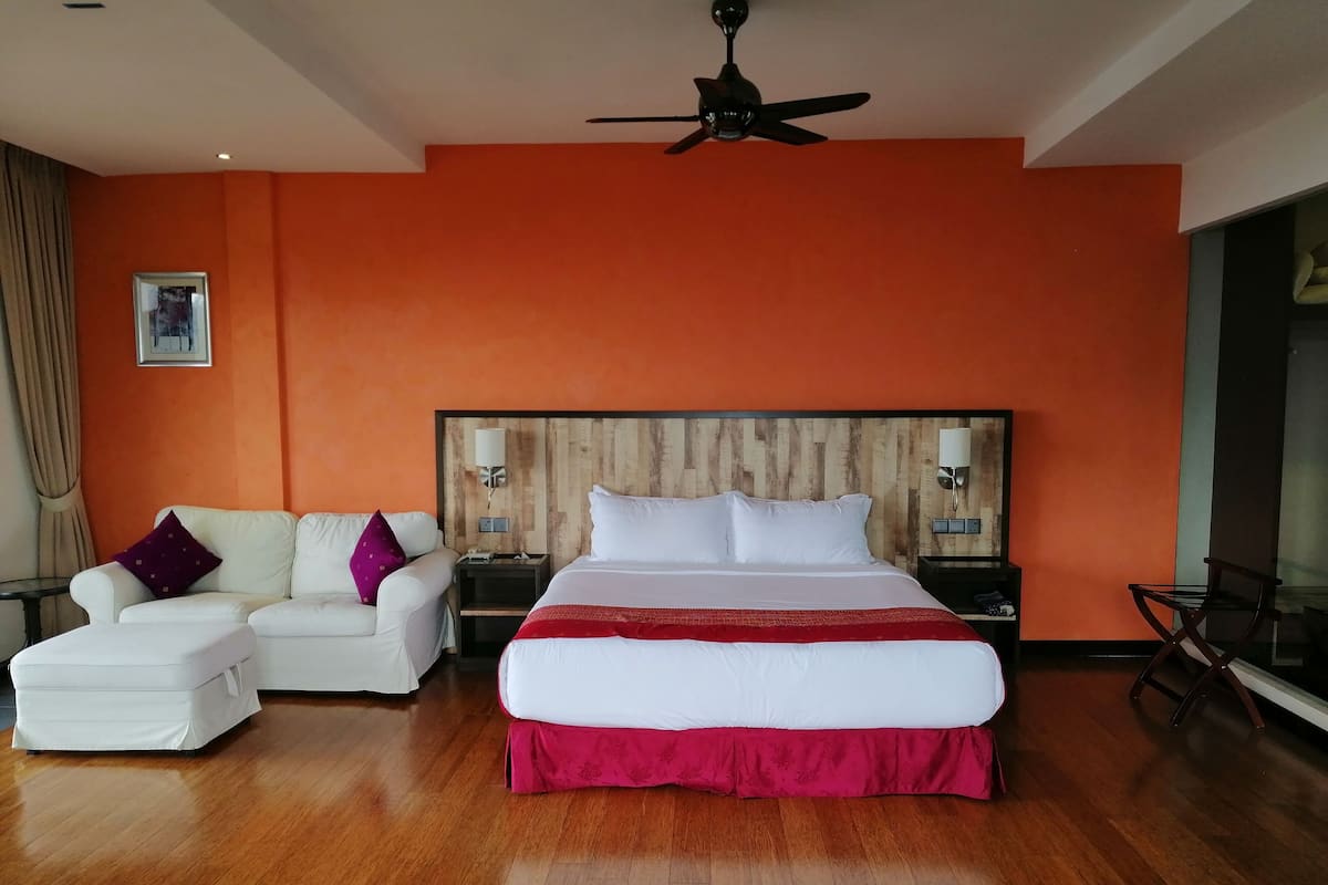 A hotel room with a large bed, a white sofa, a wooden headboard, and a ceiling fan.