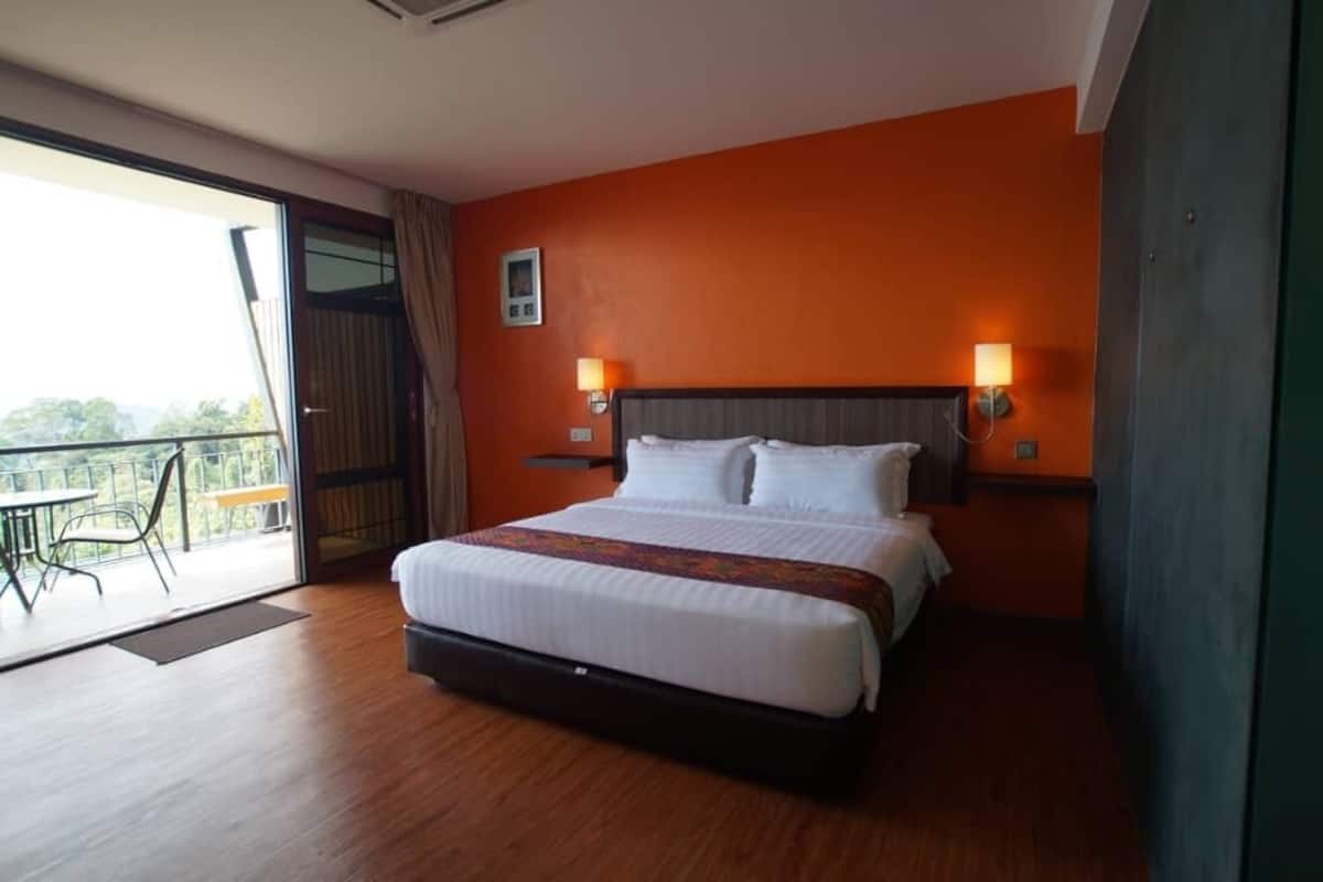 A hotel room with a large bed, two bedside lamps, a balcony with a table and chairs, and an orange wall.
