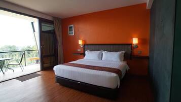 Une chambre d’hôtel avec un grand lit, deux lampes de chevet, un balcon avec une table et des chaises, et un mur de couleur orange.