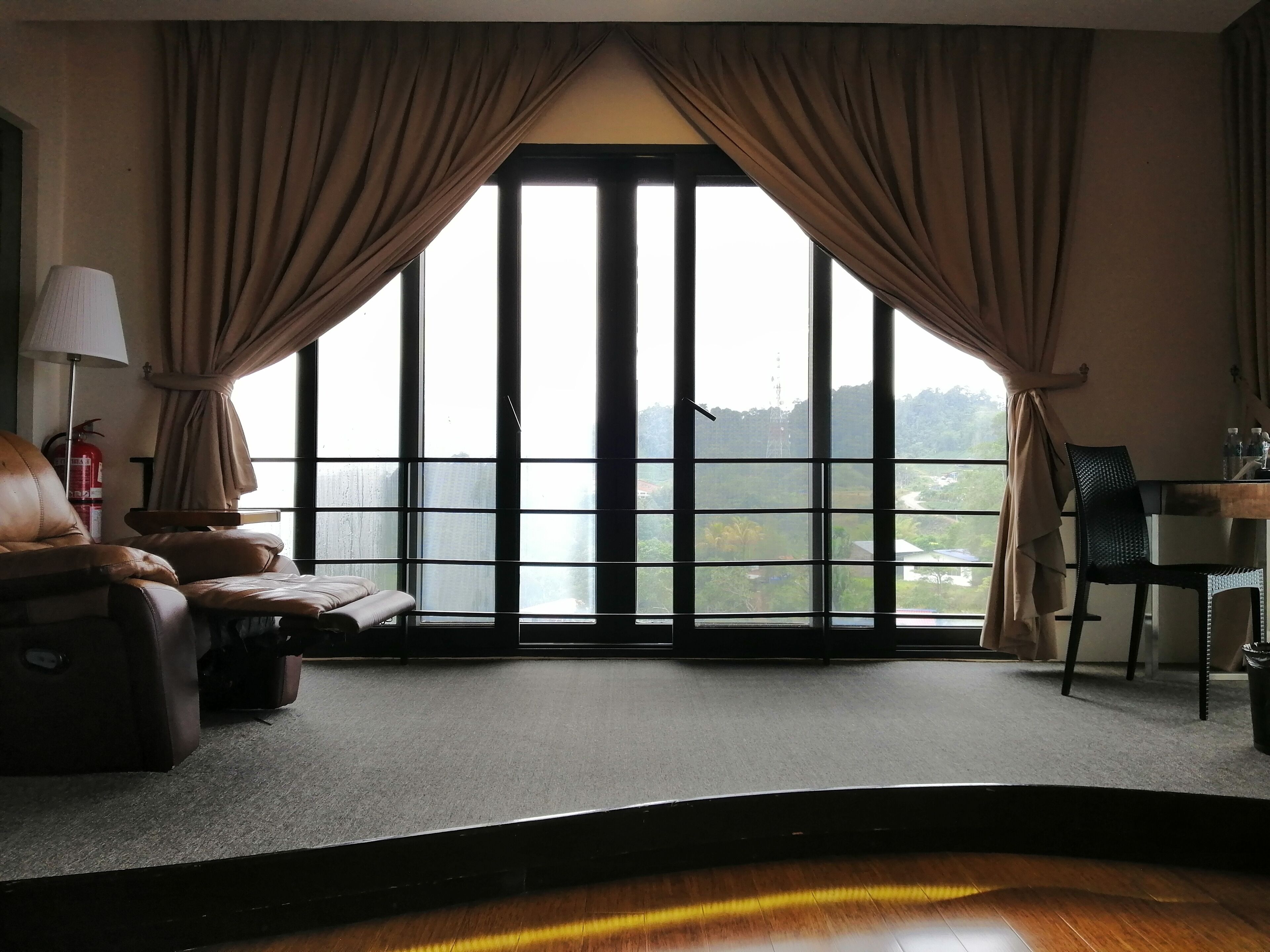 A room with a large window, a leather chair, a small table, and a lamp.