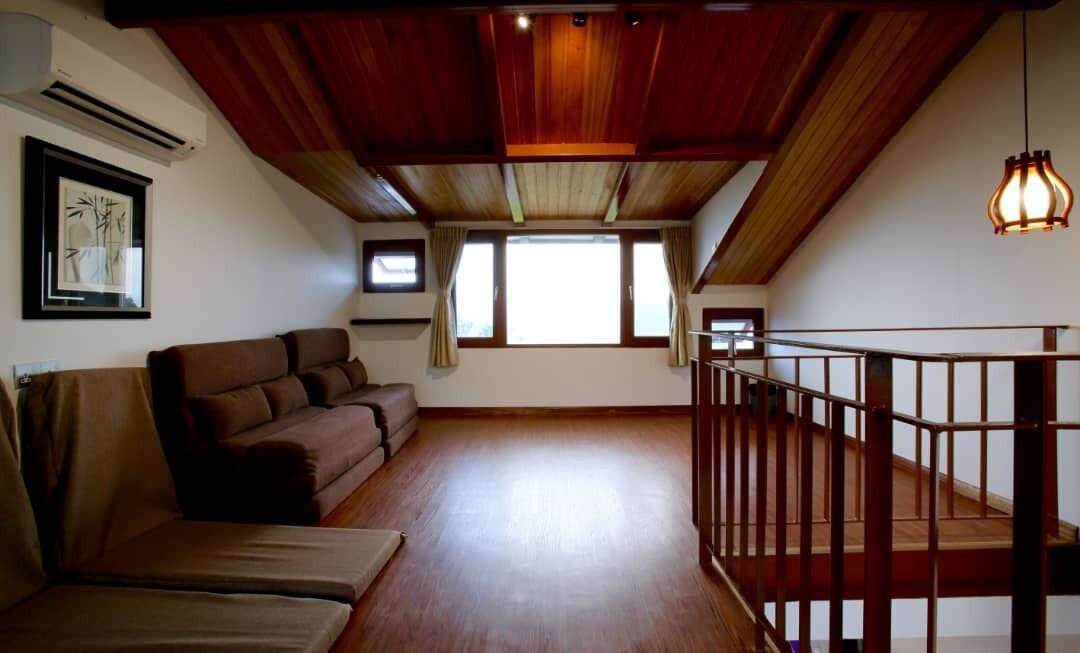 Amplia sala de estar con techo de madera, un sofá marrón, una escalera y un ventanal que deja entrar luz natural.