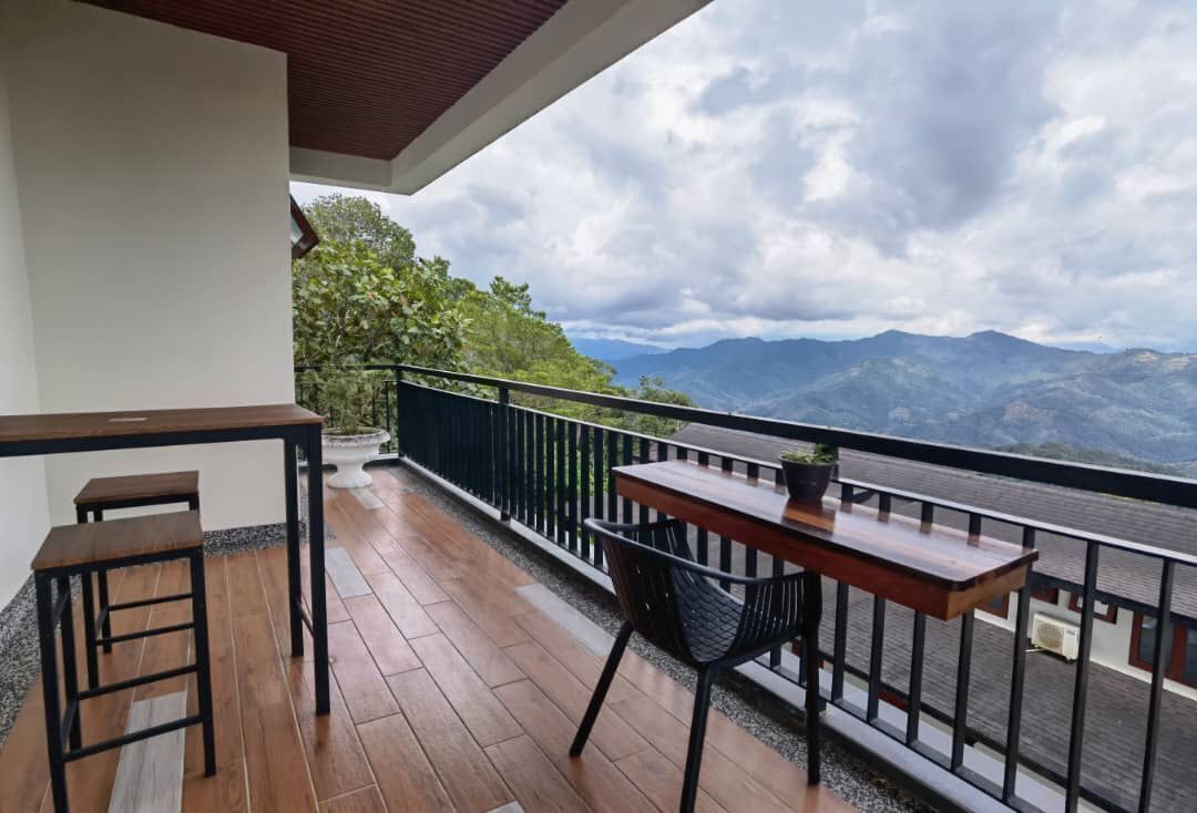 A balcony with a wooden table and two stools, overlooking a mountainous landscape.
