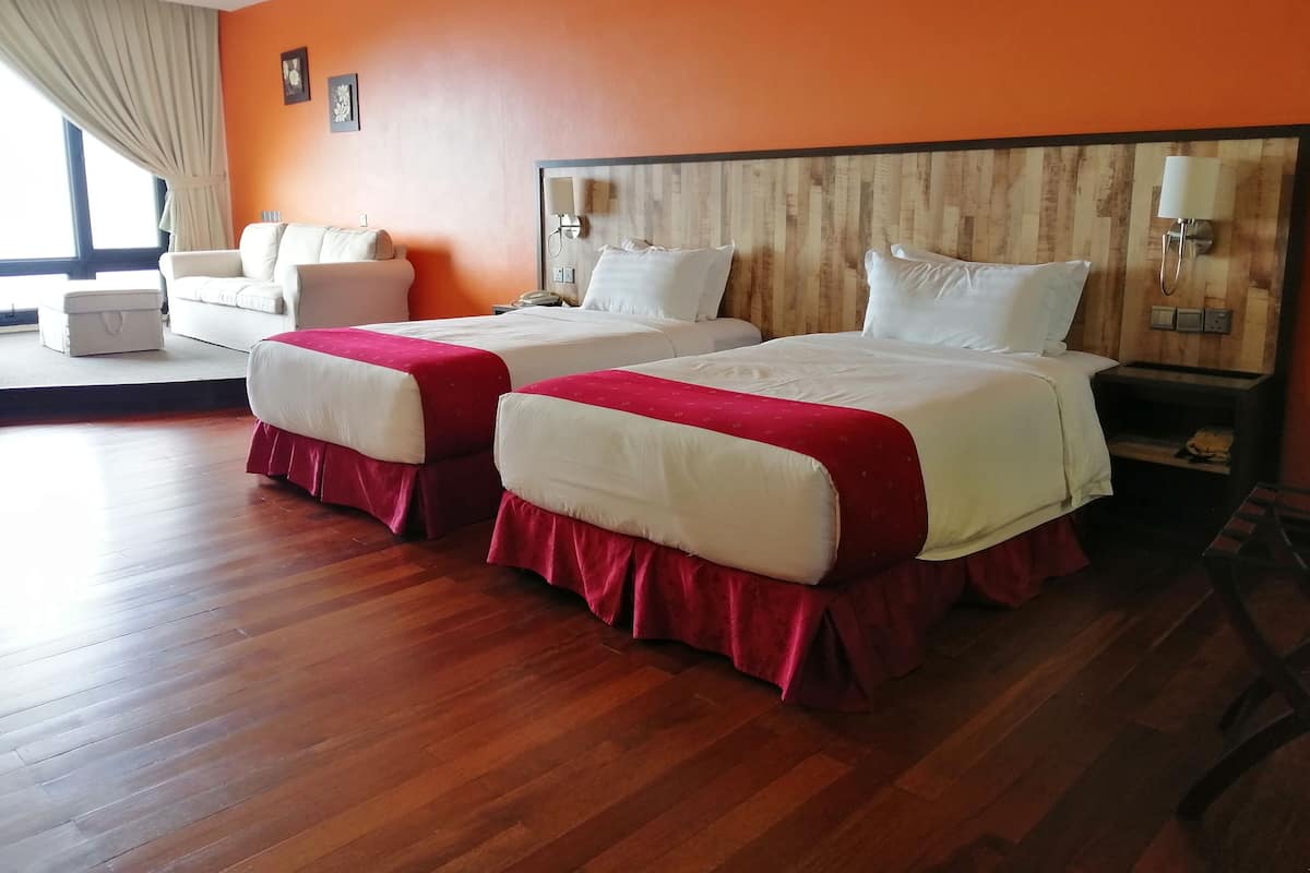 A hotel room with two beds, a sofa, a wooden headboard, and a window with curtains.
