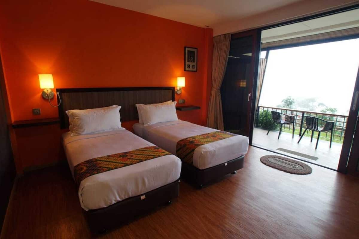 A hotel room with two beds, a balcony with chairs, and a view of the outdoors.