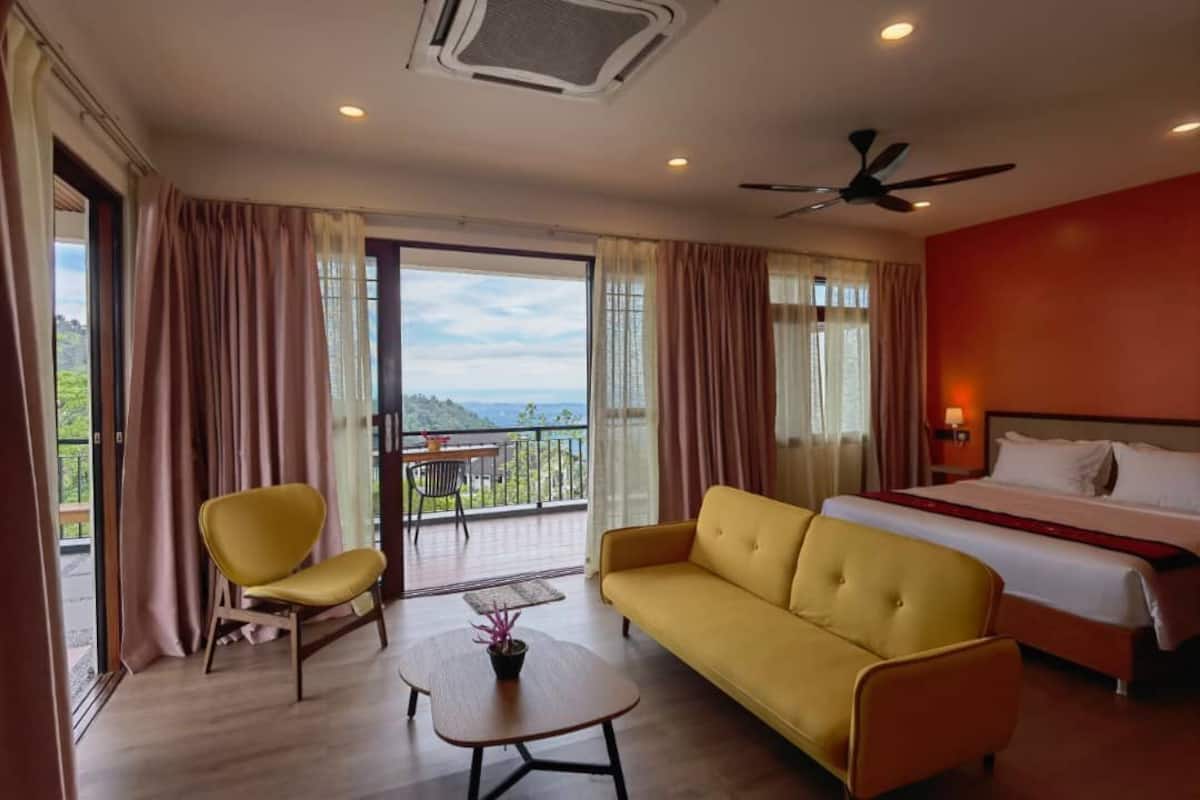 A hotel room with a bed, a yellow sofa, a small table, a chair, and a balcony with a view.