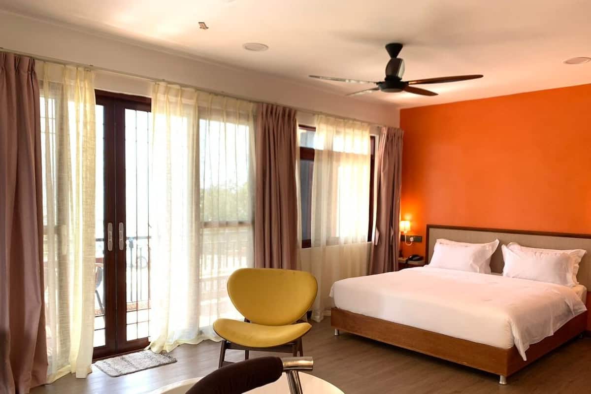 A hotel room with a bed, a yellow chair, a ceiling fan, and a view through the window.