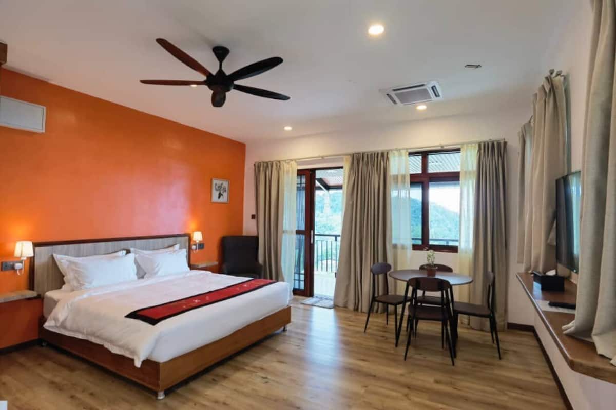 A hotel room with a bed, ceiling fan, and a balcony with a table and chairs.