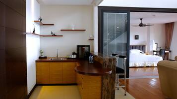 A modern hotel room with a kitchen area, a dining table, and a bed.