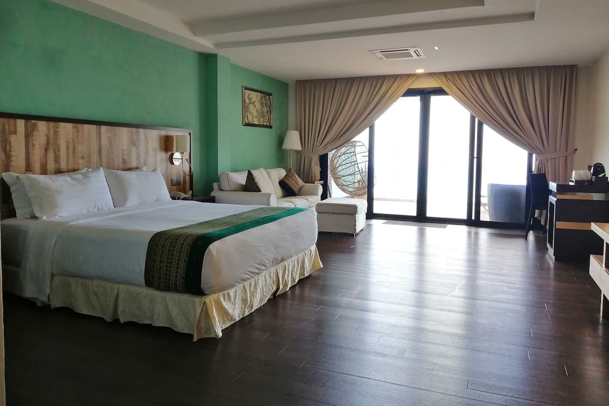 A hotel room with a large bed, a desk, and a view through large windows.