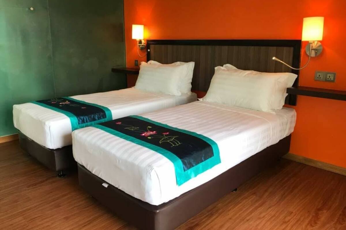A hotel room with two beds, each with white linens and teal bedspreads. There are wall-mounted lamps on either side of the beds.