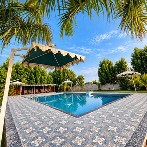 A swimming pool with a tiled deck, surrounded by palm trees and a clear sky. - The Royal Heritage Tent Resort - Statue Of Unity (Garudeshwar)