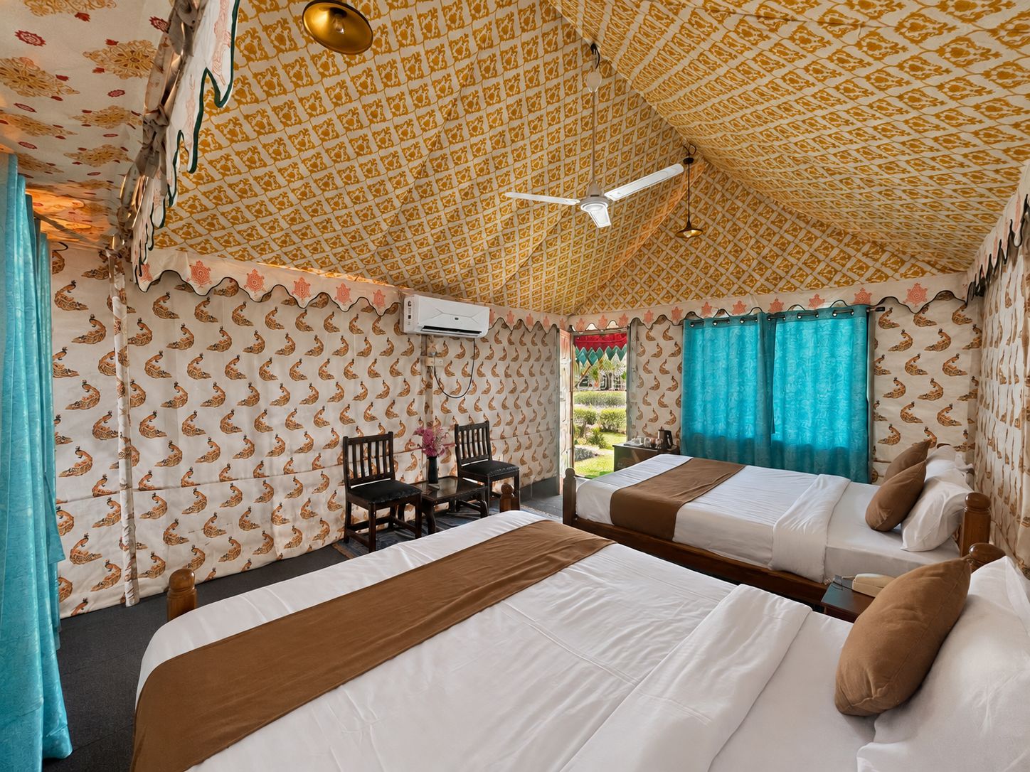 A room with two beds, a ceiling fan, an air conditioning unit, and a view of a garden.