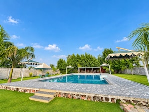 A swimming pool with a stone deck, surrounded by grass and palm trees. - The Royal Heritage Tent Resort - Statue Of Unity (Garudeshwar)
