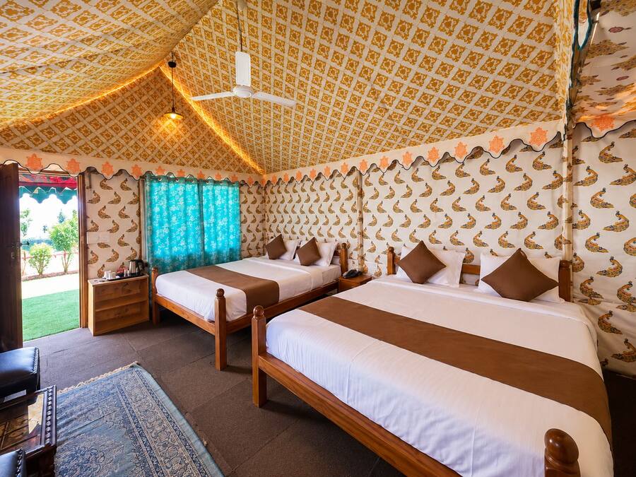 A room with two beds, a ceiling fan, patterned wallpaper, and a view of the outdoors.