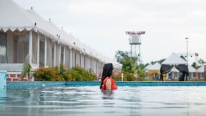 Zwembad met iemand in het water, een wit gebouw met kolommen en een watertoren op de achtergrond.