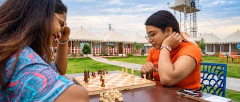 Two individuals playing chess outdoors with a clear sky and a distant sign reading 'IFC CITY'.