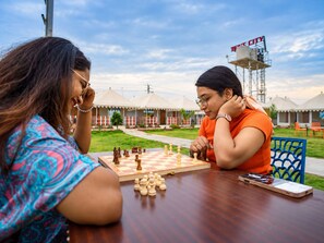 Two individuals playing chess outdoors with a clear sky and a distant sign reading 'IFC CITY'. - The Royal Heritage Tent Resort - Statue Of Unity (Garudeshwar)