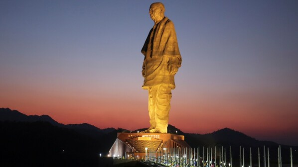 A large illuminated statue of a man standing on a platform with a backdrop of mountains and a twilight sky. - The Royal Heritage Tent Resort - Statue Of Unity (Garudeshwar)