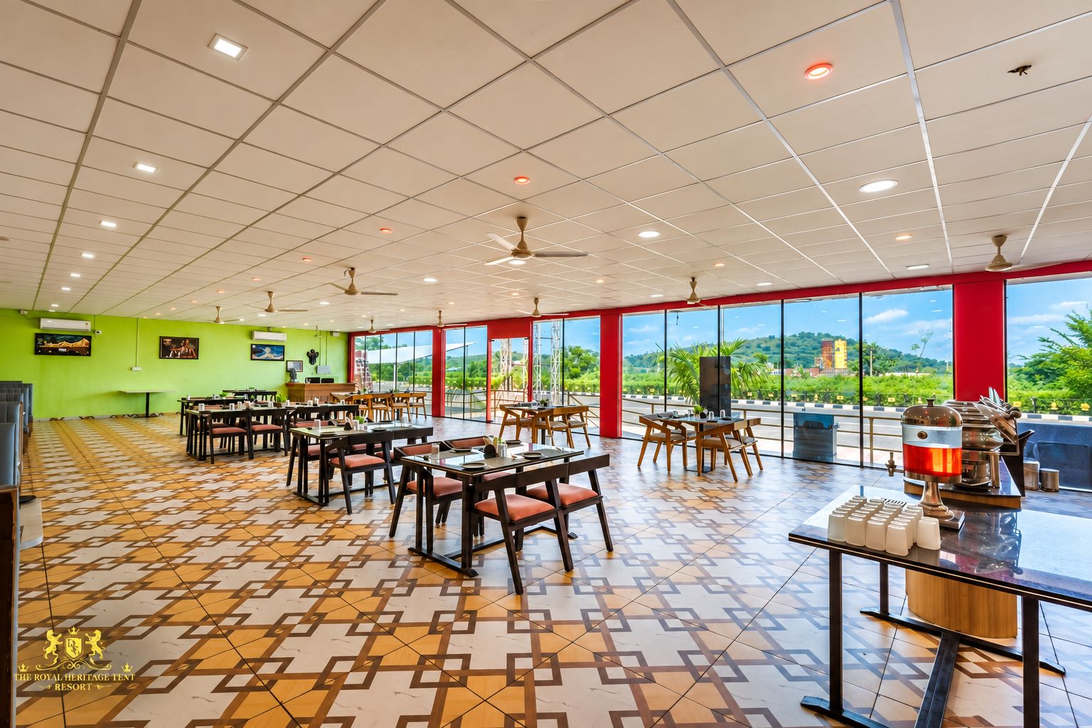 A spacious dining area with multiple tables and chairs, large windows offering a view of the outdoors, and a ceiling with recessed lighting and fans.
