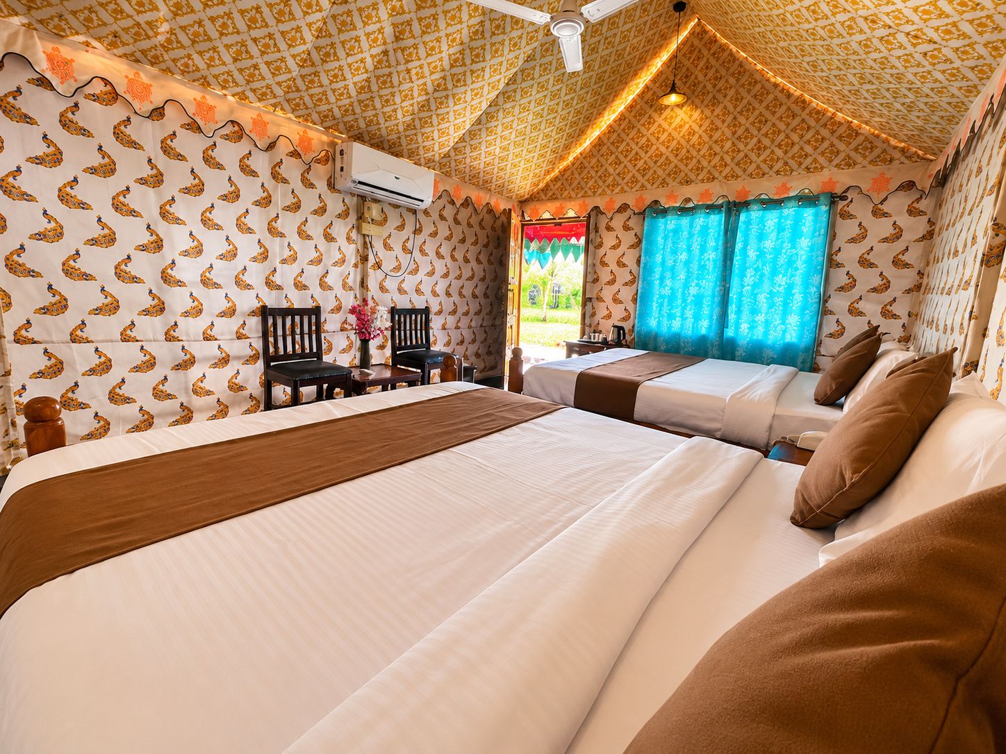 A hotel room with two beds, a ceiling fan, and patterned wallpaper.