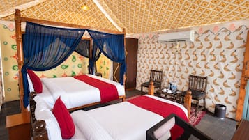 A room with two beds, a wooden headboard, a small table with chairs, and patterned wallpaper.