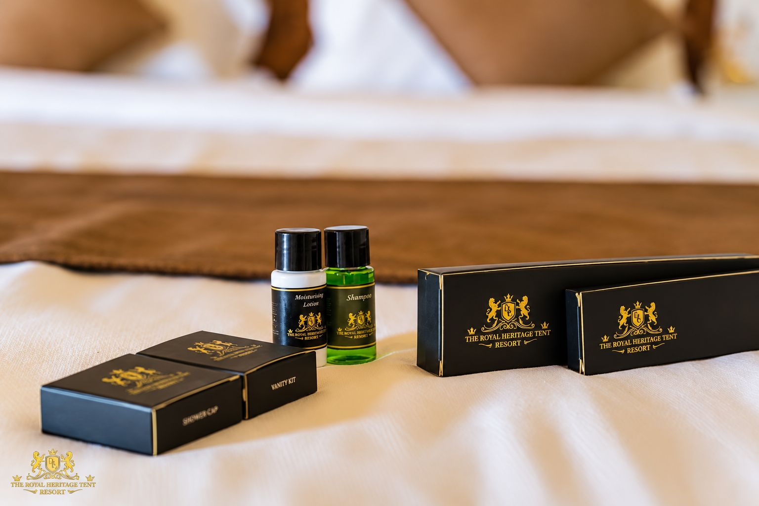 Una cama con una manta marrón, dos cajas negras con emblemas dorados, una botella verde y una botella negra con emblemas dorados.