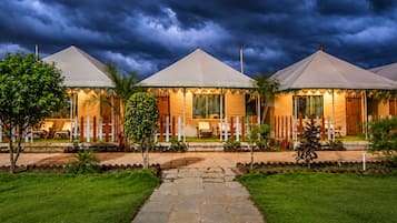 A row of three tents with a stone pathway leading to them, surrounded by grass and trees.