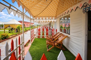 Een overdekt terras met een patroonluifel, een wit en rood hekwerk en uitzicht op een gebouw op de achtergrond.
