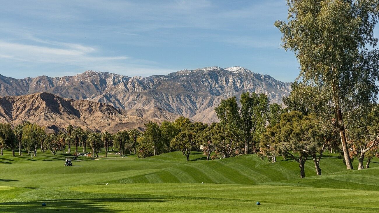 Ein Golfplatz vor dem Hintergrund von Bergen, Bäumen und einem klaren Himmel.