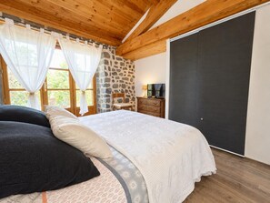 Une chambre à coucher avec un lit, un mur en pierre, une télévision et une armoire.