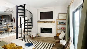 A modern living room with a black spiral staircase, a fireplace, a dining area with a striped rug, and a bookshelf. - Penthouse Cozy Condo in the heart of Downtown Winter Park (Winter Park)