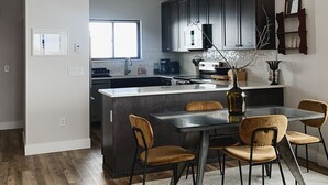 A modern kitchen with dark cabinets, a central island, and a chandelier. - Penthouse Cozy Condo in the heart of Downtown Winter Park (Winter Park)