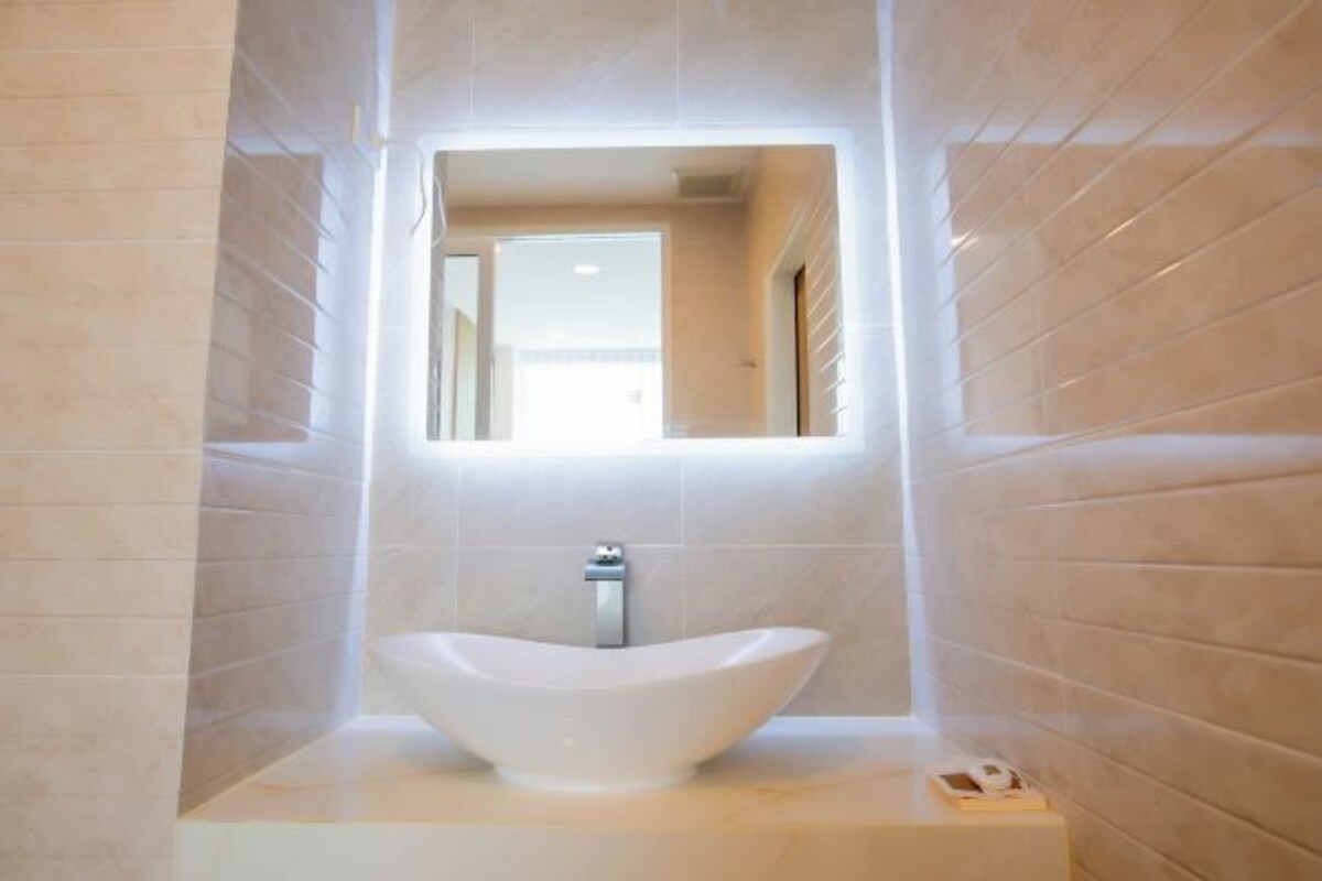 Un baño moderno con un lavamanos grande, blanco y con forma de cuenco, situado en un pedestal y rodeado de baldosas beiges.