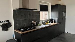 A modern kitchen with black cabinets, a wooden countertop, a gas stove, and a window providing natural light. - Christinahoeve Apartment #8 (Boskoop)