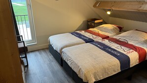 A bedroom with a large bed, a nightstand, a wooden shelf, a window with a view of a green field, and a ceiling light. - Christinahoeve Apartment #8 (Boskoop)