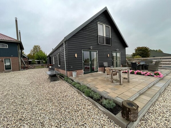 A two-story house with a dark exterior, a balcony, and a patio area with outdoor furniture.