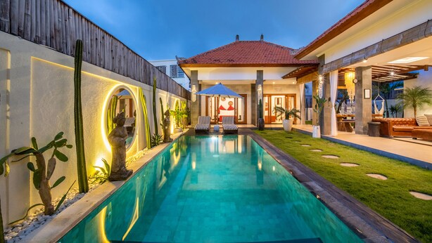 A swimming pool with lounge chairs and a statue, surrounded by a well-maintained lawn and a wooden fence. - Cozy 3br Villa with Pool in Canggu (Canggu)