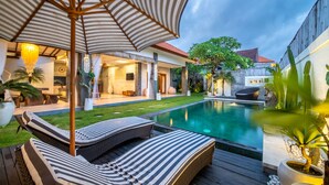 A poolside area with lounge chairs and an umbrella, a well-maintained lawn, and a wooden deck. - Cozy 3br Villa with Pool in Canggu (Canggu)