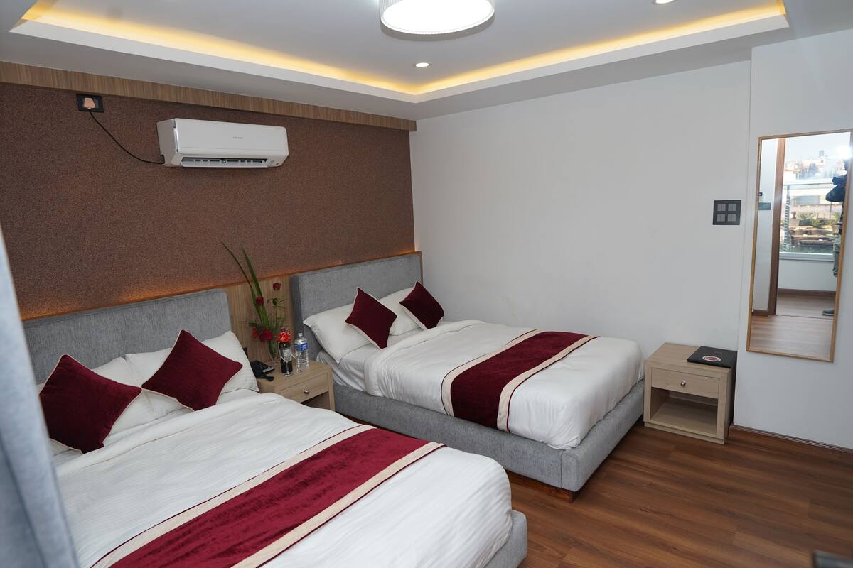 A hotel room with two beds, a nightstand, a lamp, and a mirror.