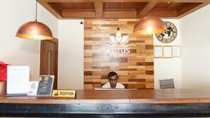 A reception desk with a wooden panel wall, a clock, and a lotus symbol. - Lotus Club Boutique Hotel (Tarakeshwar)