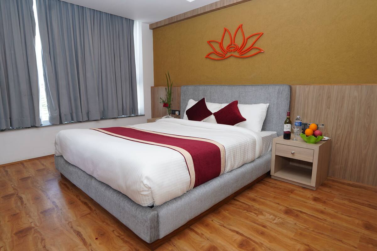 A neatly made bed with a red and white bedspread, a wooden nightstand with a bottle and fruit, and a wall with a lotus flower decoration.