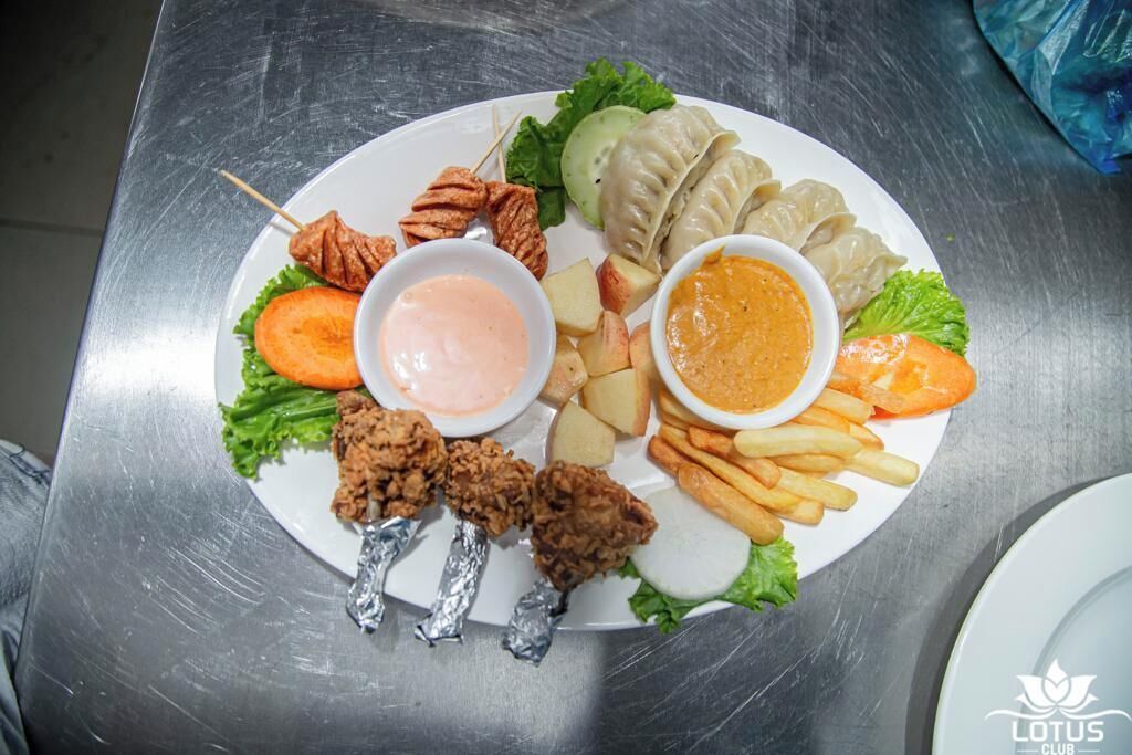 A plate of food including fried chicken, dumplings, fries, and vegetables with dipping sauces.