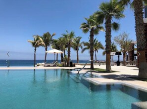 Área de piscina com palmeiras, cadeiras de descanso e vista para o oceano.